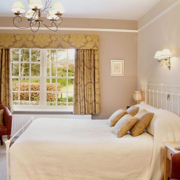 a picture of a cream room with gold and light brown decor including cushions and curtains, with a view of hedges outside of the window