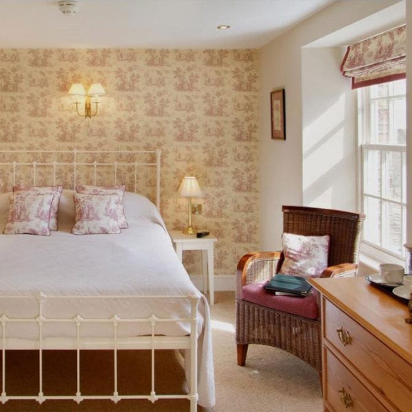 a picture of a cream bedroom with a white bed, a red and cream wallpaper with red and cream patterned cushions