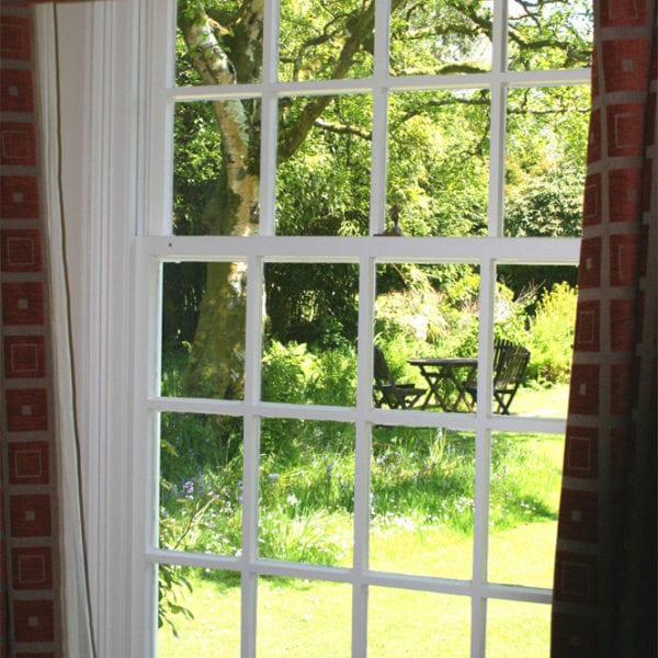 a picture of a window with a view of the garden, trees and garden furniture outside