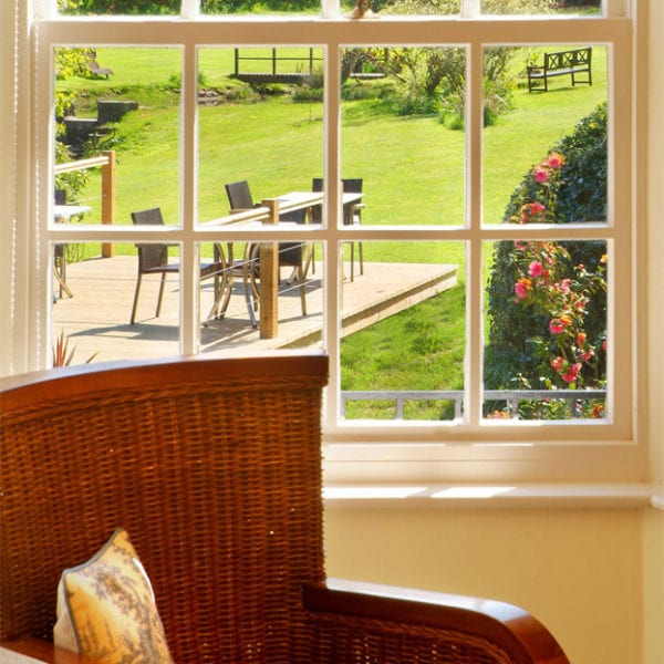 a picture of a brown wicker chair with stacked magazines, and a view from a bedroom window out into the garden with garden furniture