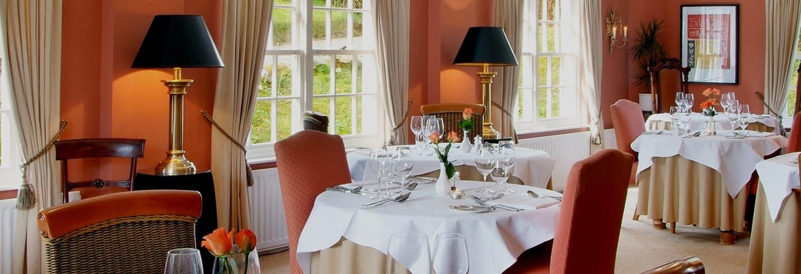 a picture of a terracotta dining room, with laid dining room tables with glassware and orange tulips in vases