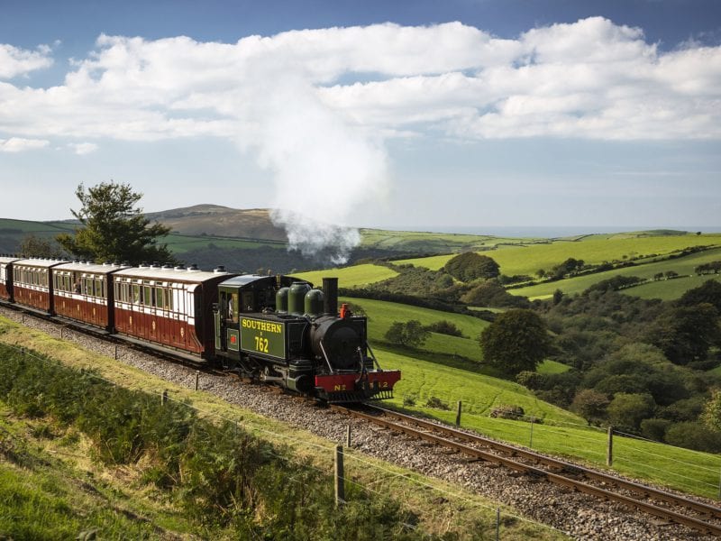 a picture of a steam train rolling through the countryside from woody bay station