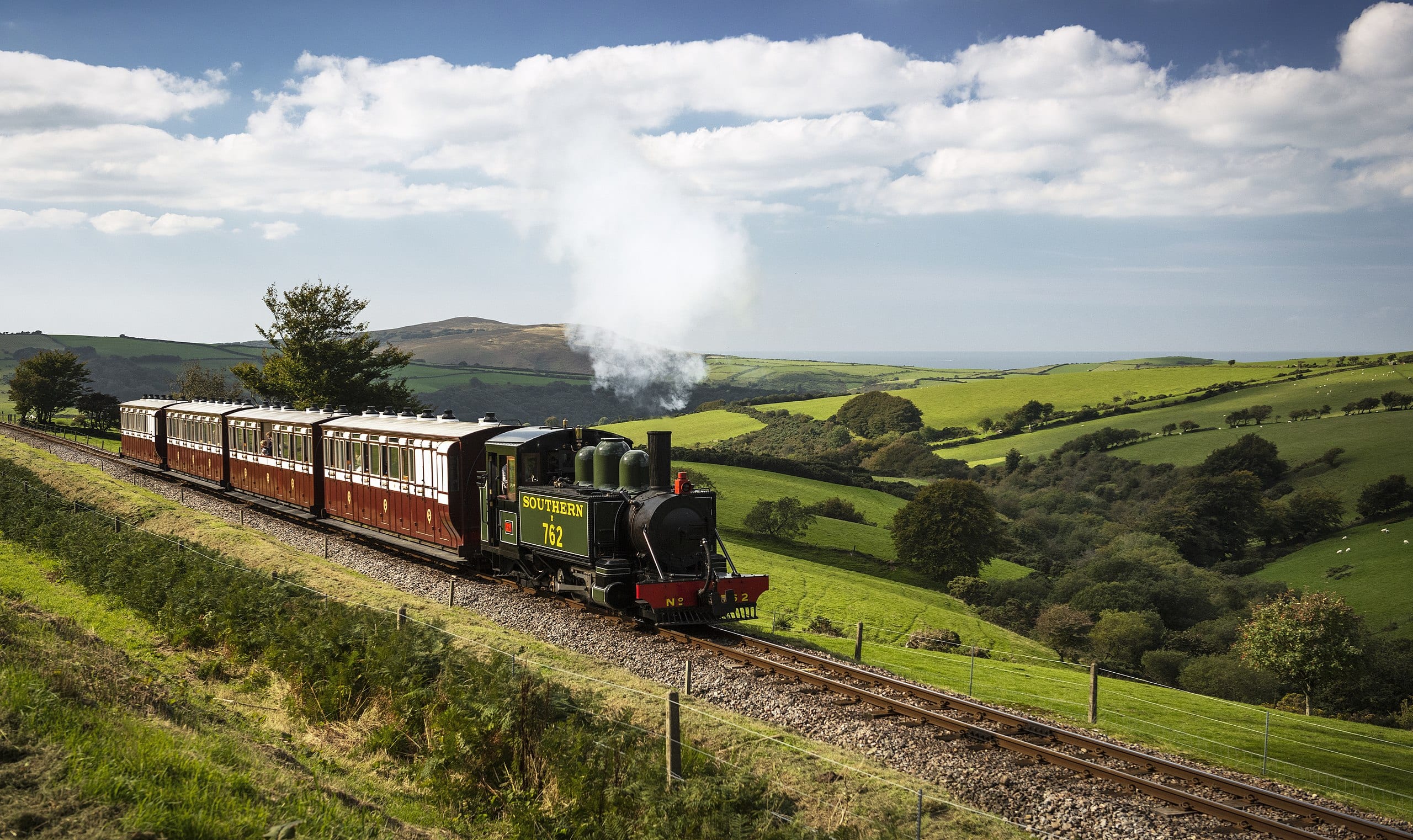 a picture of a steam train rolling through the countryside from woody bay station