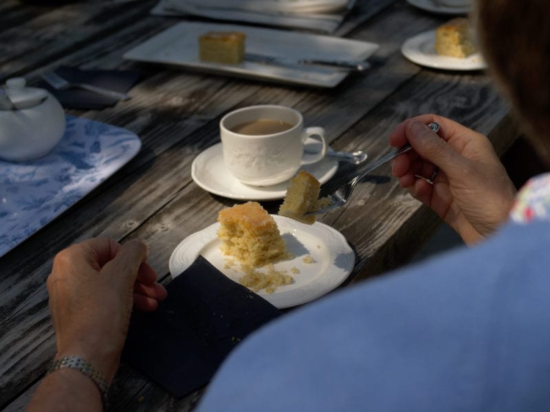 a picture of someone eating a Victoria sponge cake outside on a bench with a cup of tea