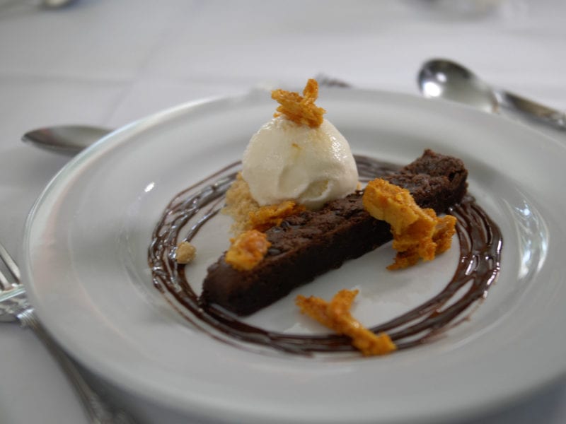 a picture of a strip of brownie cake toped with honeycomb, ice cream and surrounded by chocolate sauce