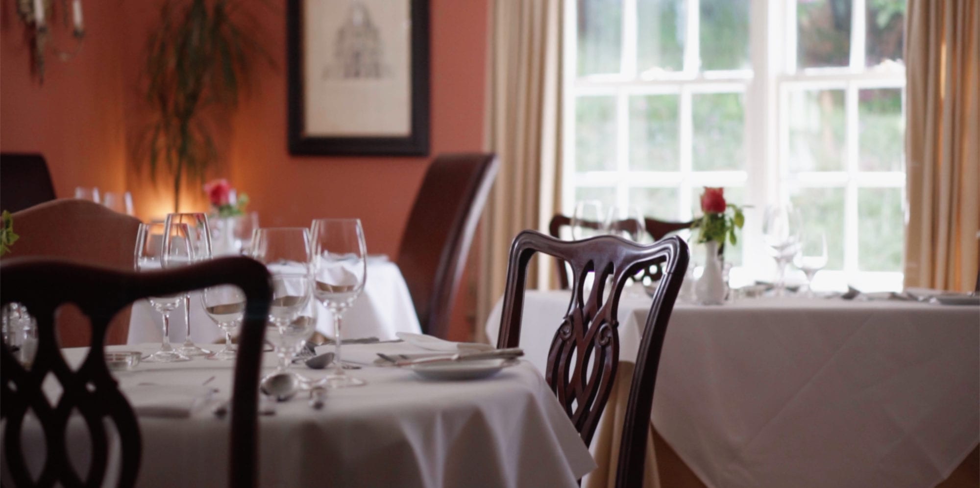 a picture of a laid table in a dining rooms, with glass wear and roses in vases