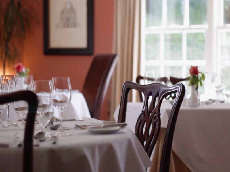 a picture of a laid table in a dining rooms, with glass wear and roses in vases