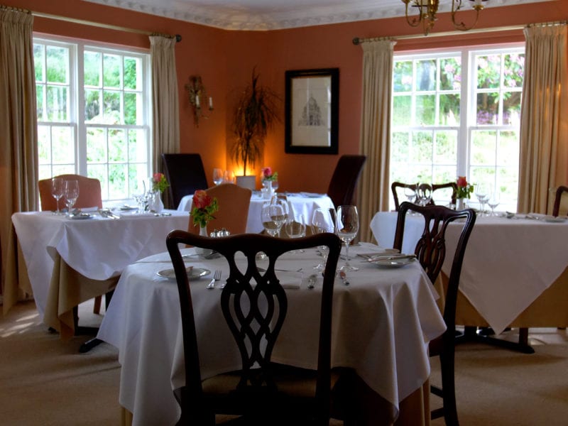 a picture of a dining room with terracotta walls, cream curtains and set tables with glass wear and flowers