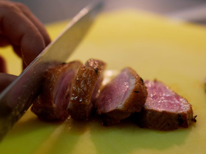 a picture of someone slicing up a cooked duck breast with a knife