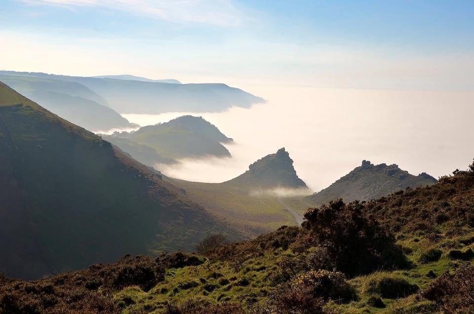 a picture of rocky green covered hills over looking the sea with clouds hovering over