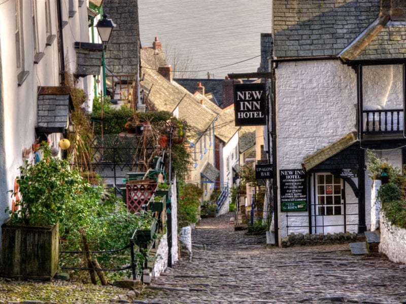 a picture of a downhill view of clovelly with white brick buildings, plants and a sea view