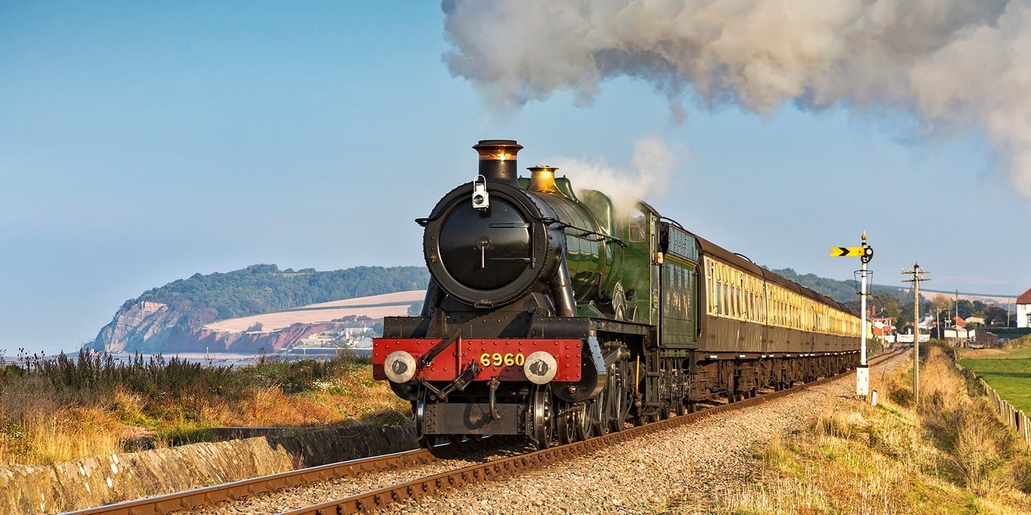 a picture of a train running through the countryside next to the coast