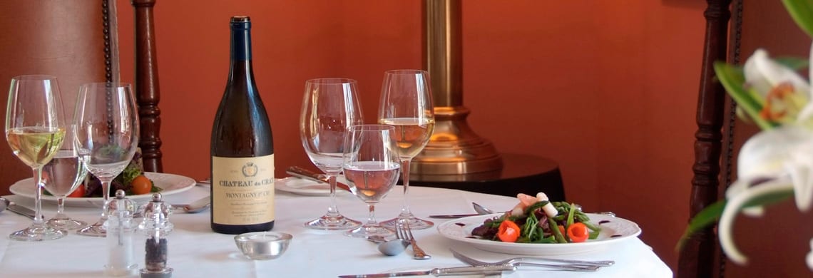 a picture of a terracotta dining room with a laid table, a plate of salad, glasses and a bottle of wine