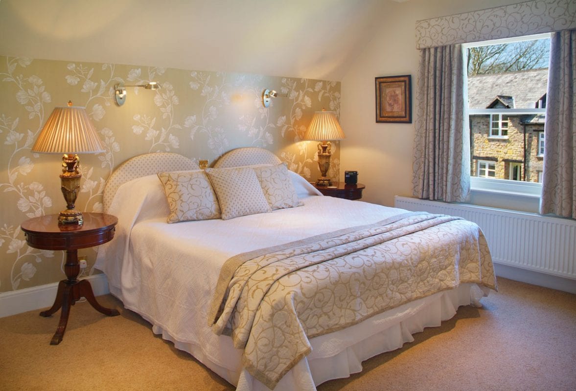 a picture of a cream bedroom with a pale green white flower feature wall, with a view of a cottage out of the window