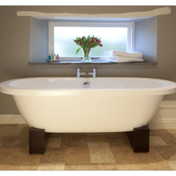 A picture of a large freestanding bath tub on dark brown stands, with a vase of pink tulips on the above shelf