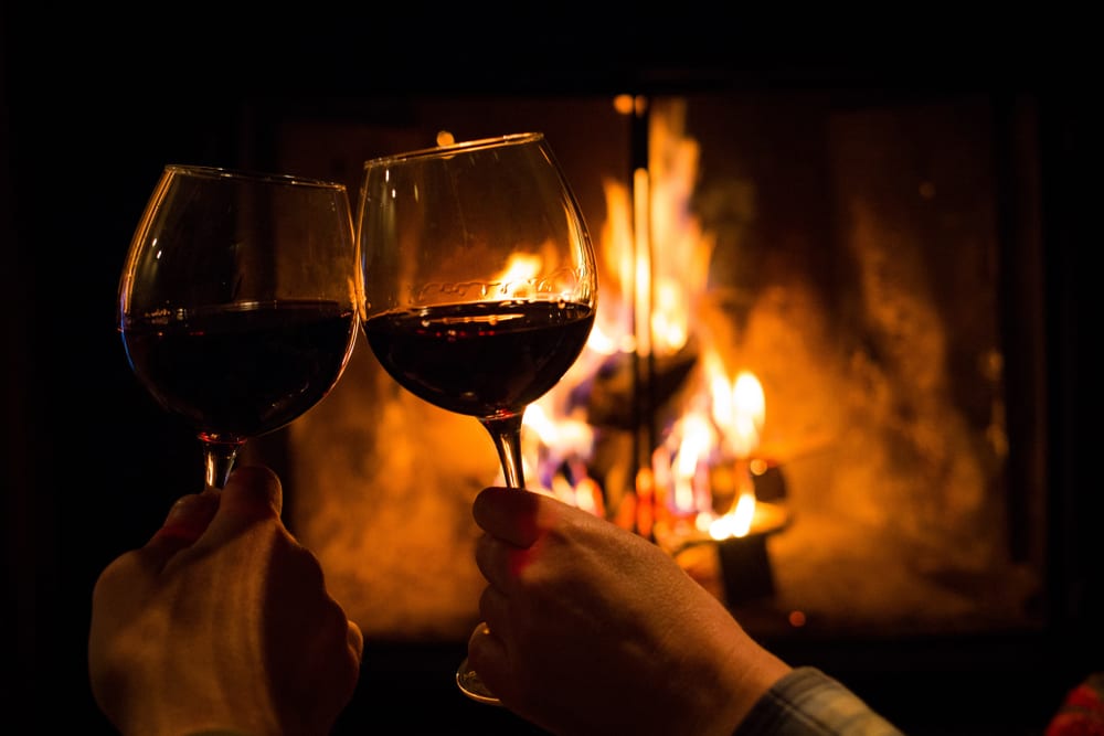 a picture of two people clinking two glasses of red wine together infront of a fire